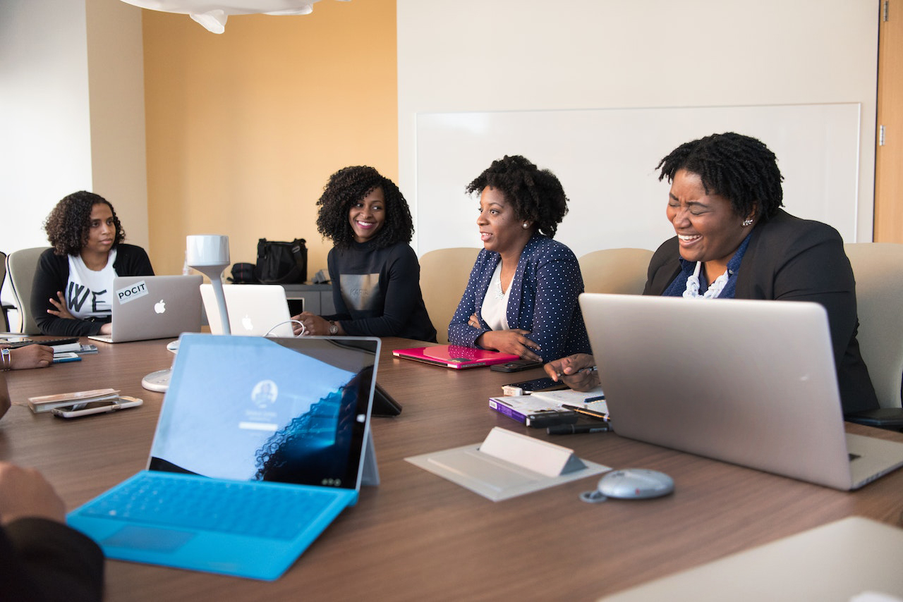 Women laugh in a meeting, board room with laptops