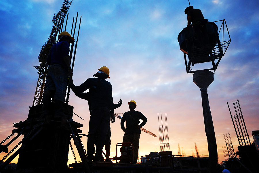 Construction workers on a building site silhouetted by a sunrise