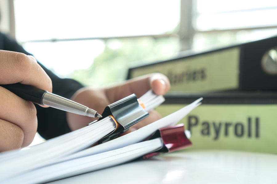 Hands, pen, paper with binder clips, binder reading "payroll"