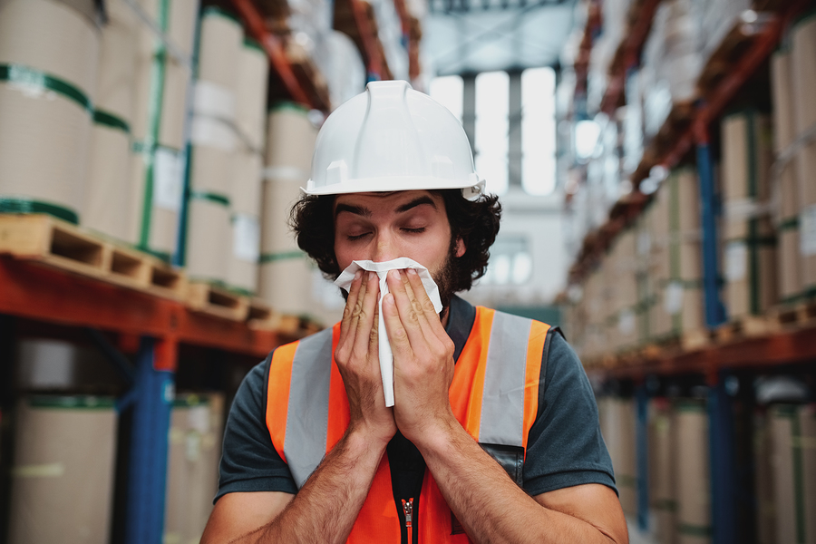 Warehouse worker in hardhat coughing into a tissue