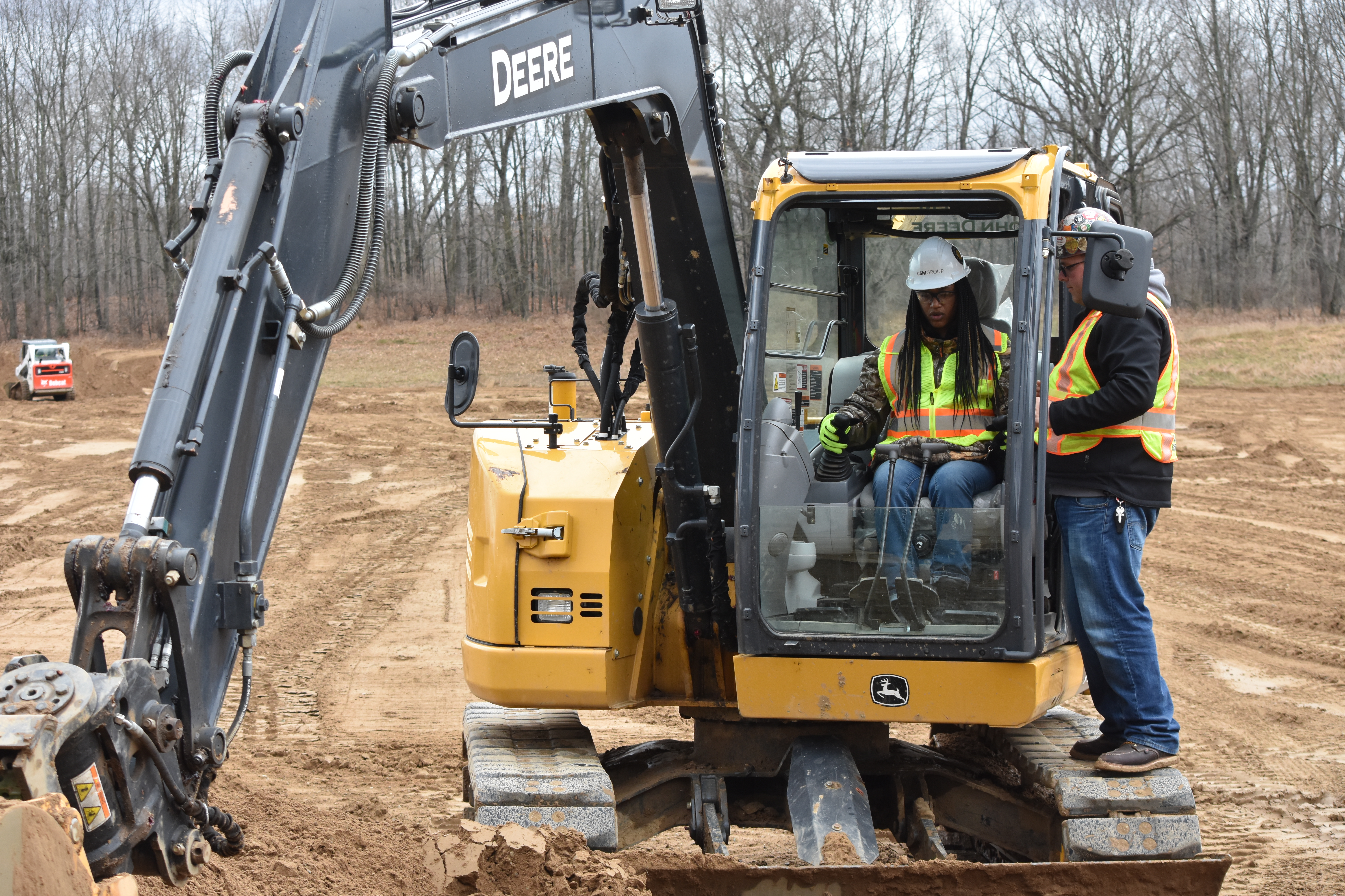 Operator instructs another operator on the controls of a backhoe