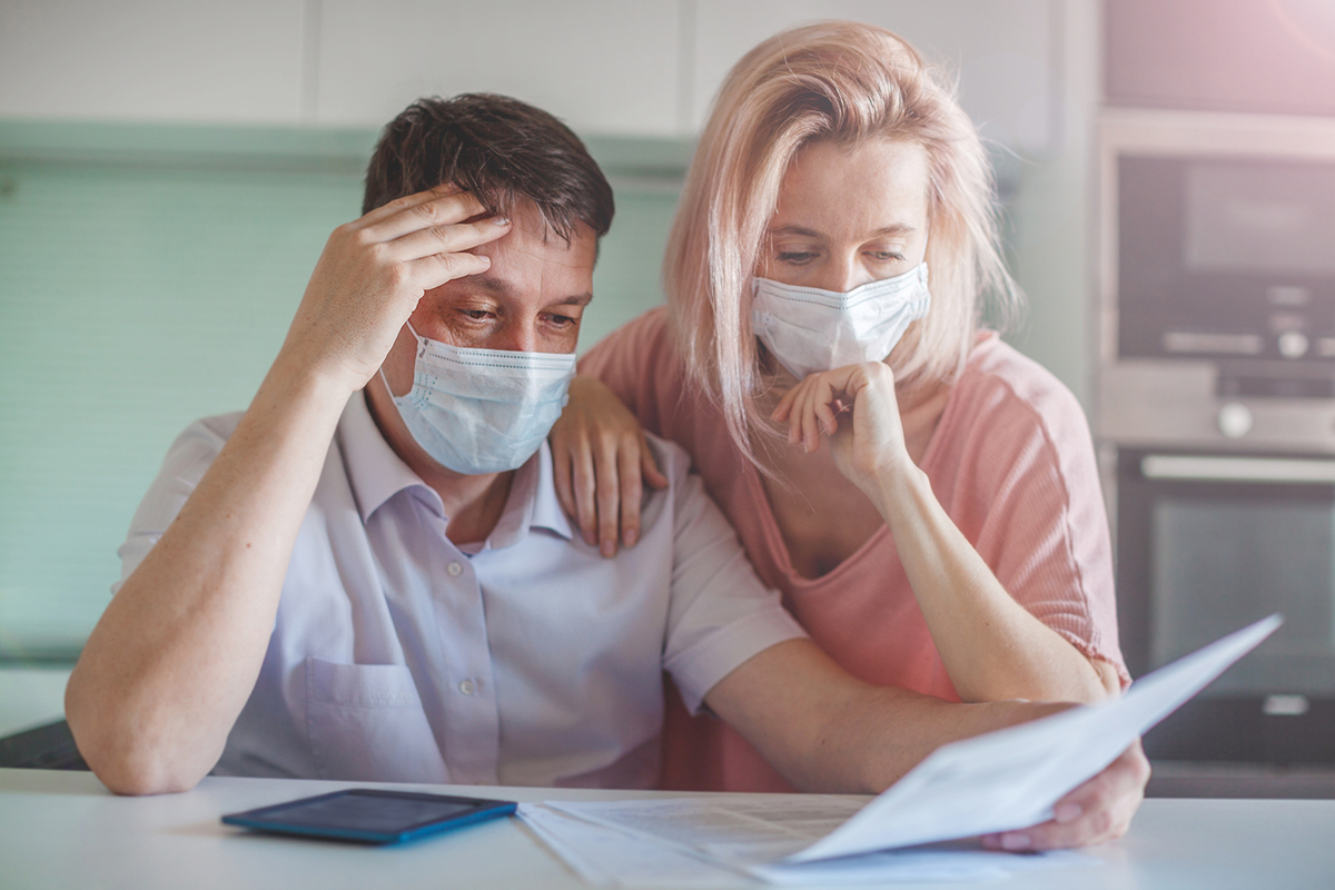 A mask-wearing couple examine their medical bills in light of the loss of a job with employer-sponsored health insurance