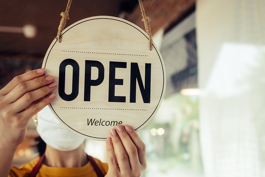 Business reopens after COVID-19 pandemic and worker flips "open" sign on shop