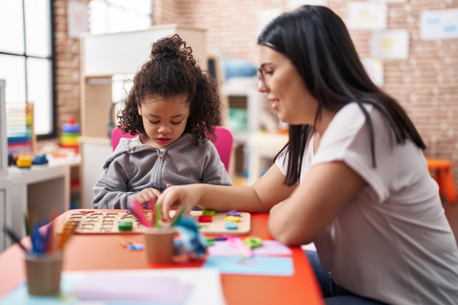 Daycare teacher works on puzzle with child. Image krakenimages.com