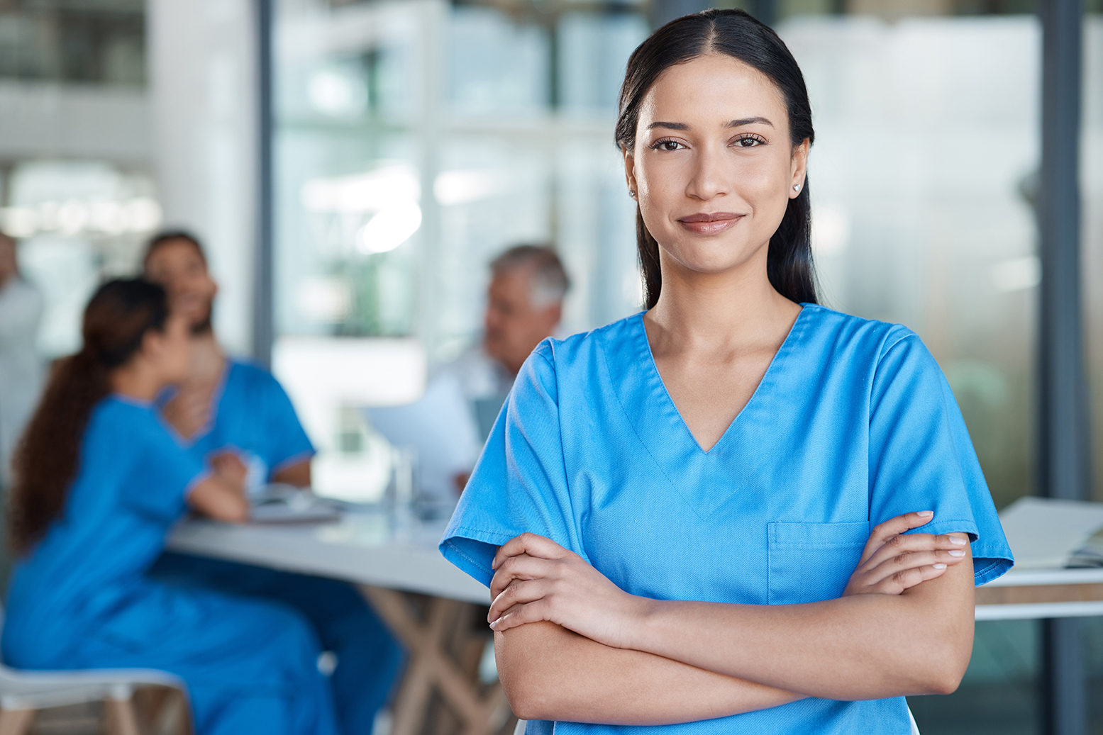 A nurse in the foreground faces the camera with other hospital workers in the background