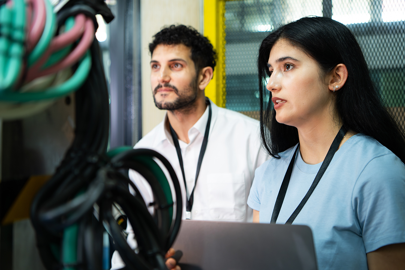 Woman and man check operations of factory at laptop with robotic arm