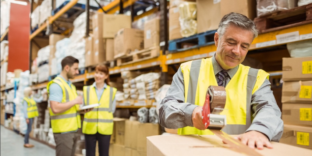 Older man in high-viz vest contentedly packing boxes in a warehouse