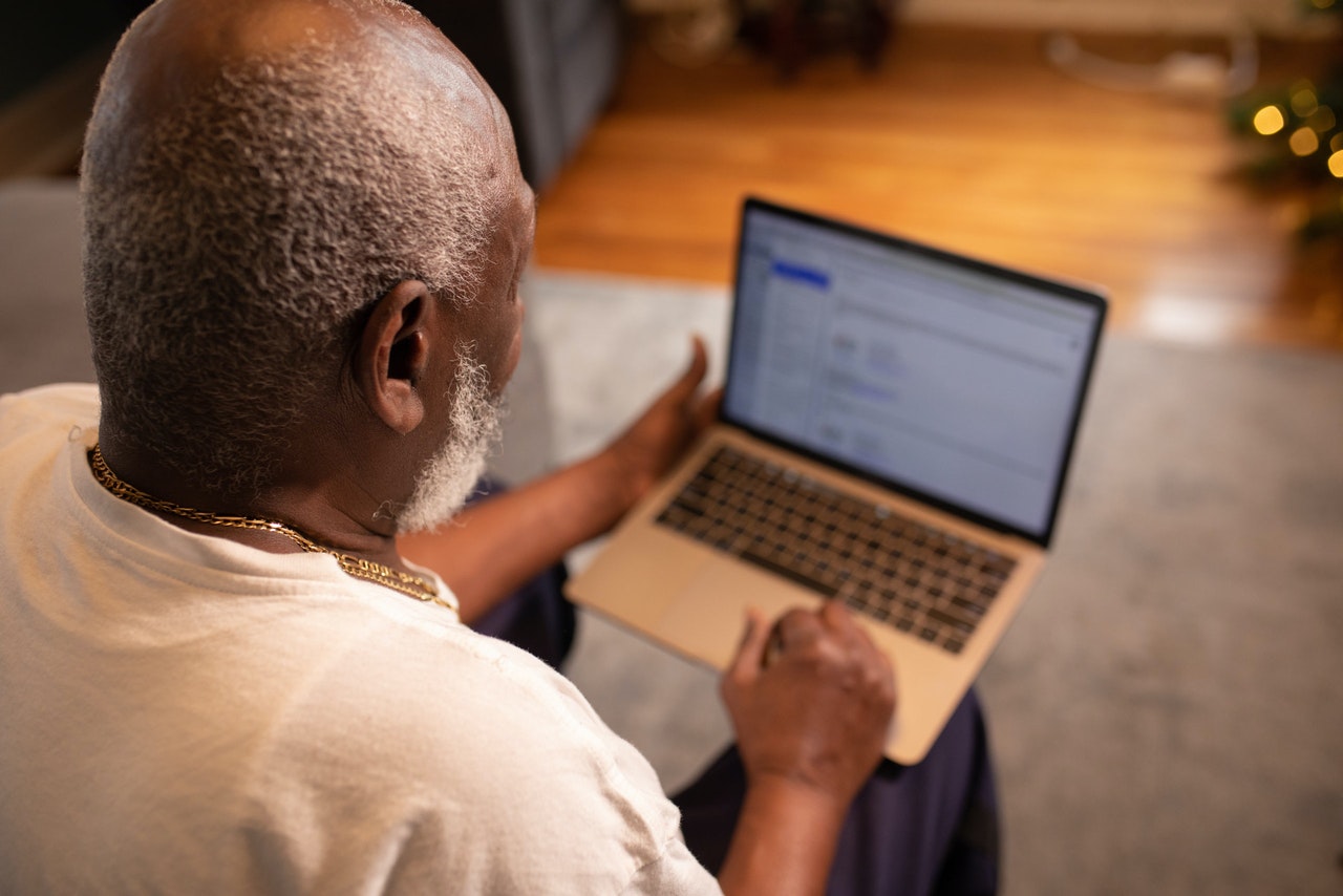 Older African-American man seen from behind with laptop computer searching for job