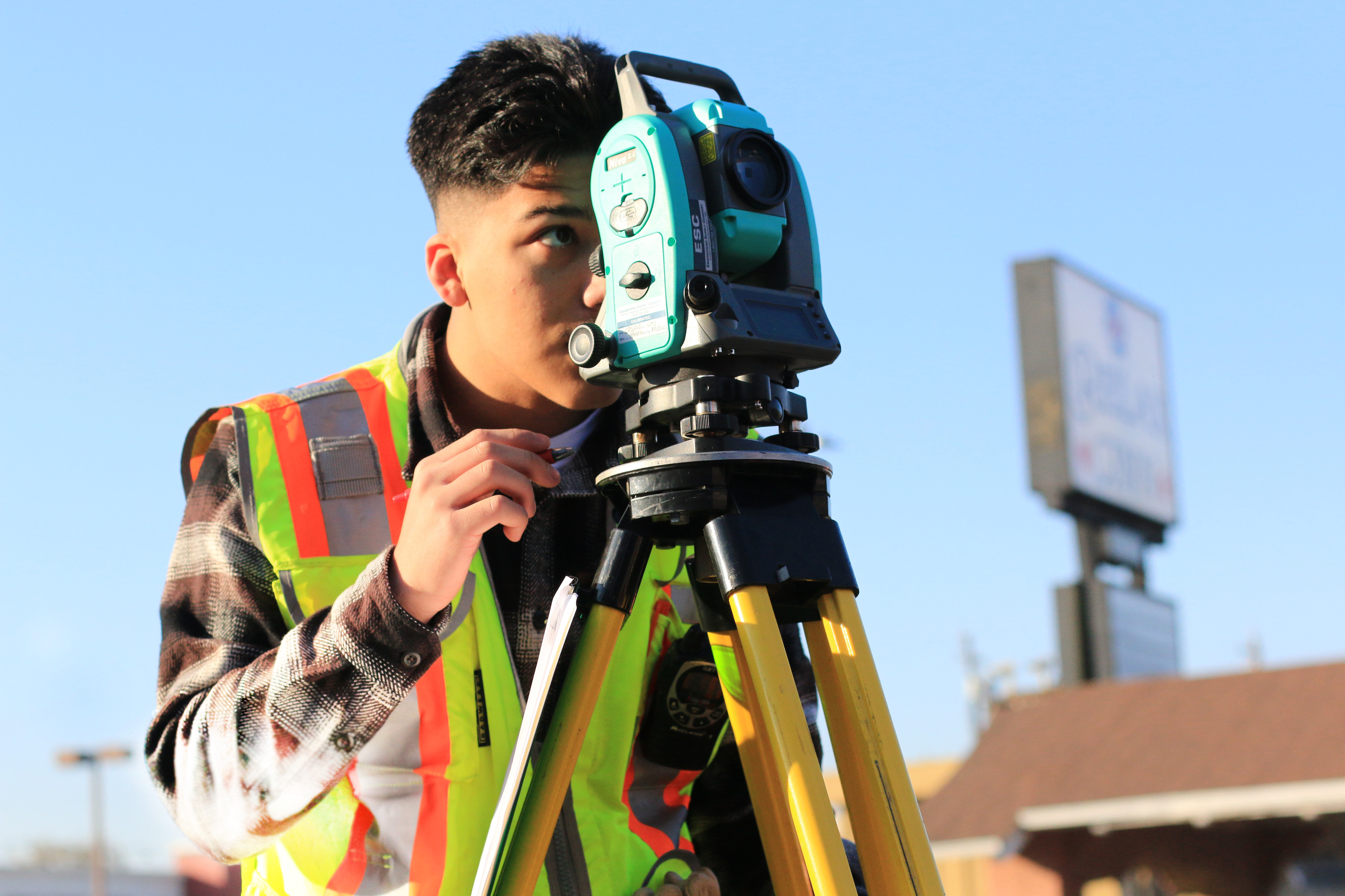 Young man surveyor in high-visibility vest looks through total station on tripod