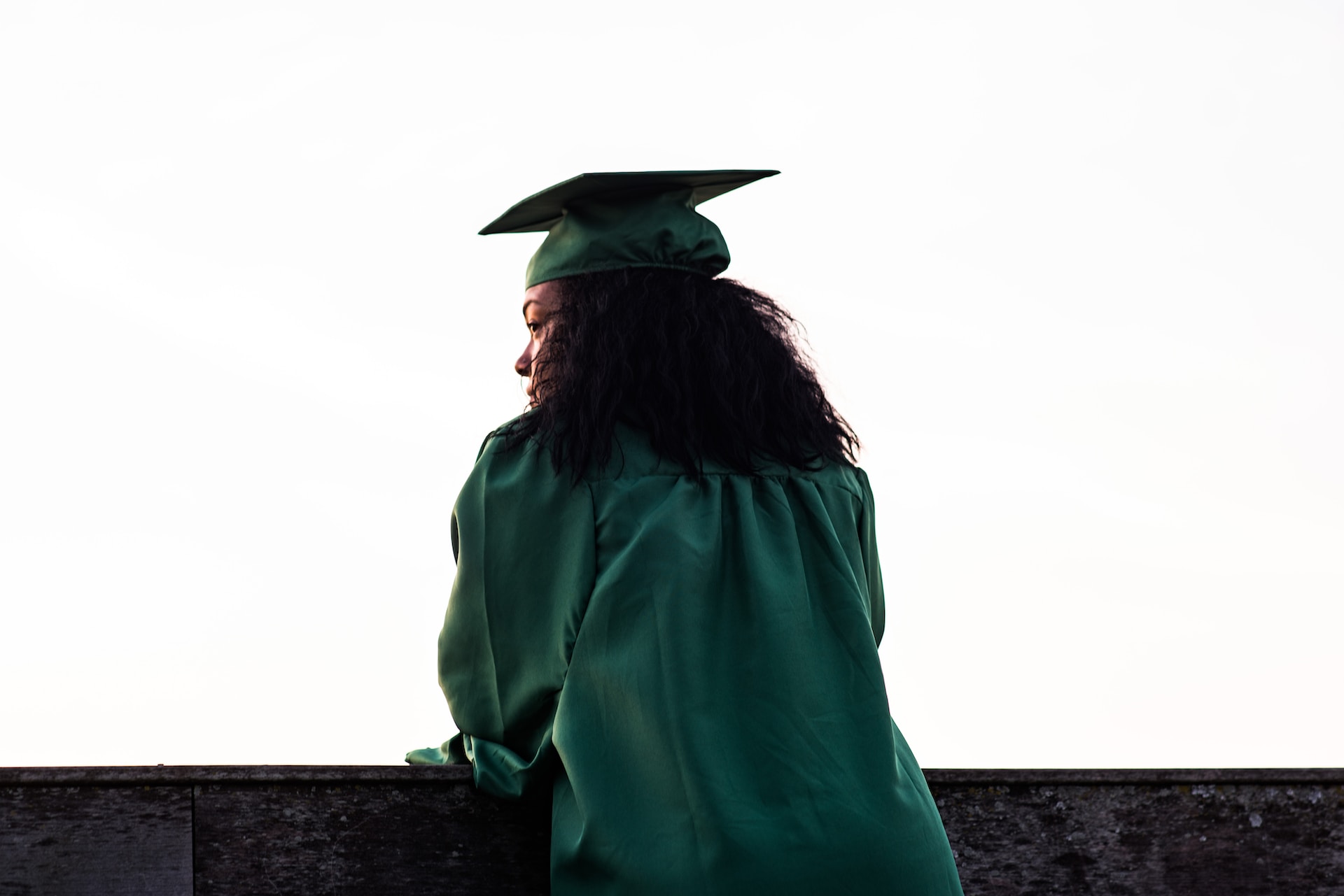 Graduate in regalia looks out over a ledge into the distance