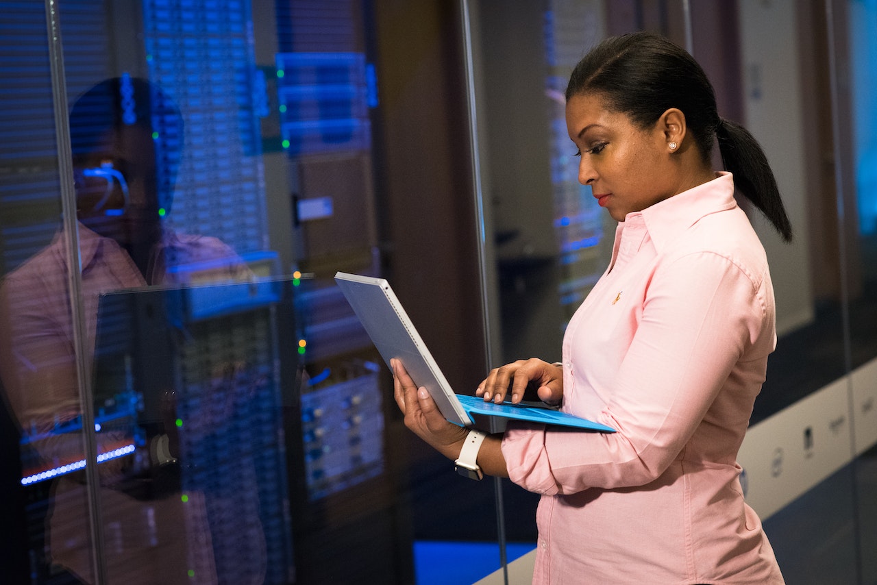 Businesswoman in pink suit checks laptop in server room