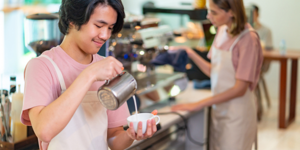A young person makes a latte in a cafe