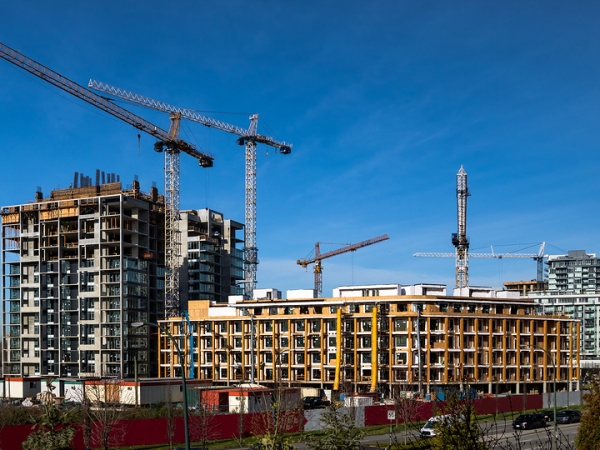 Wide view of multifamily residential construction sites in a city with multiple cranes against a blue sky