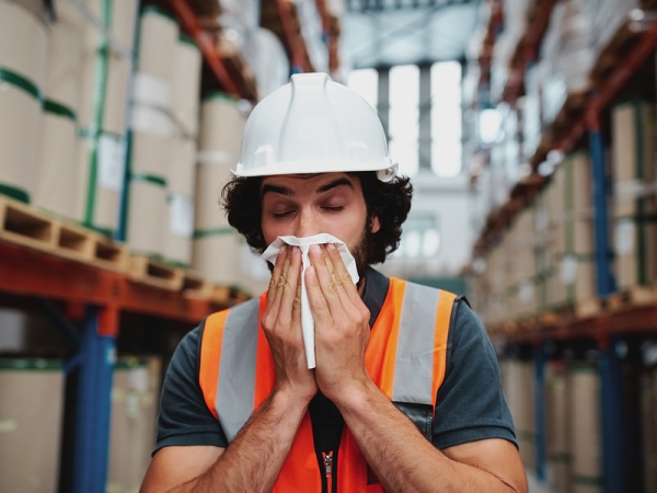 Warehouse worker in hardhat coughing into a tissue