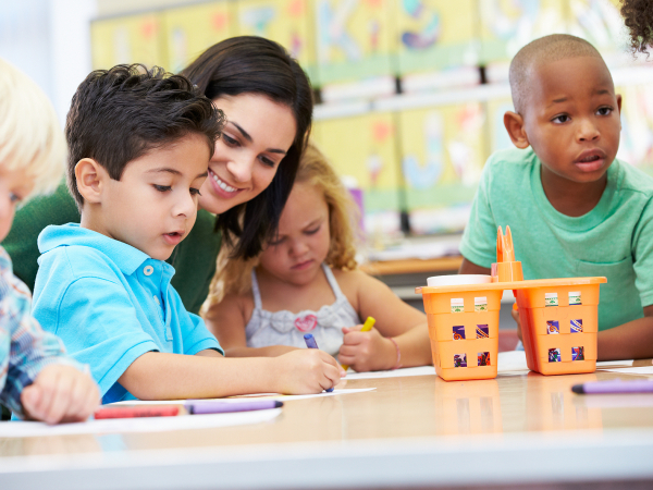 Children in a day care playing at a table. A teacher can be seen with them. 