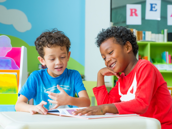 Two young children at a desk. The room they are in is vibrantly colored. 