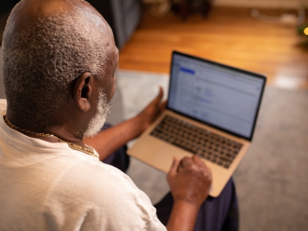Older African-American man seen from behind with laptop computer searching for job
