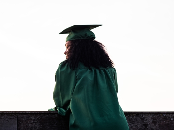 Graduate in regalia looks out over a ledge into the distance