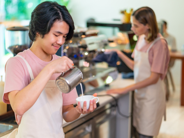 A young person makes a latte in a cafe